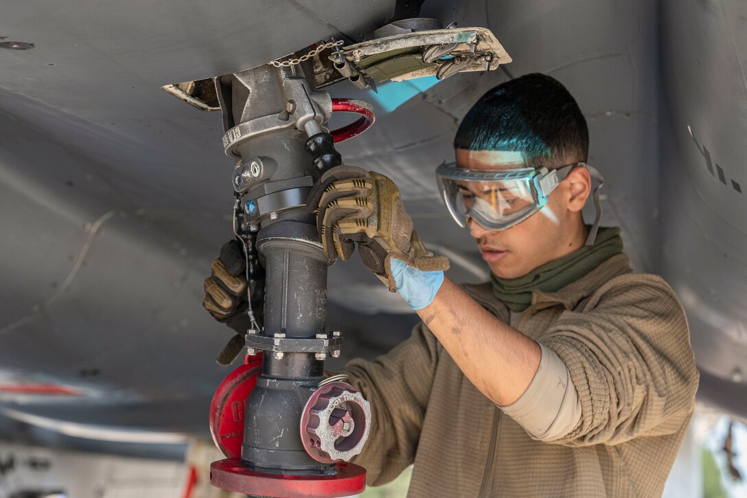 An airman attaches a fuel hose to an aircraft.