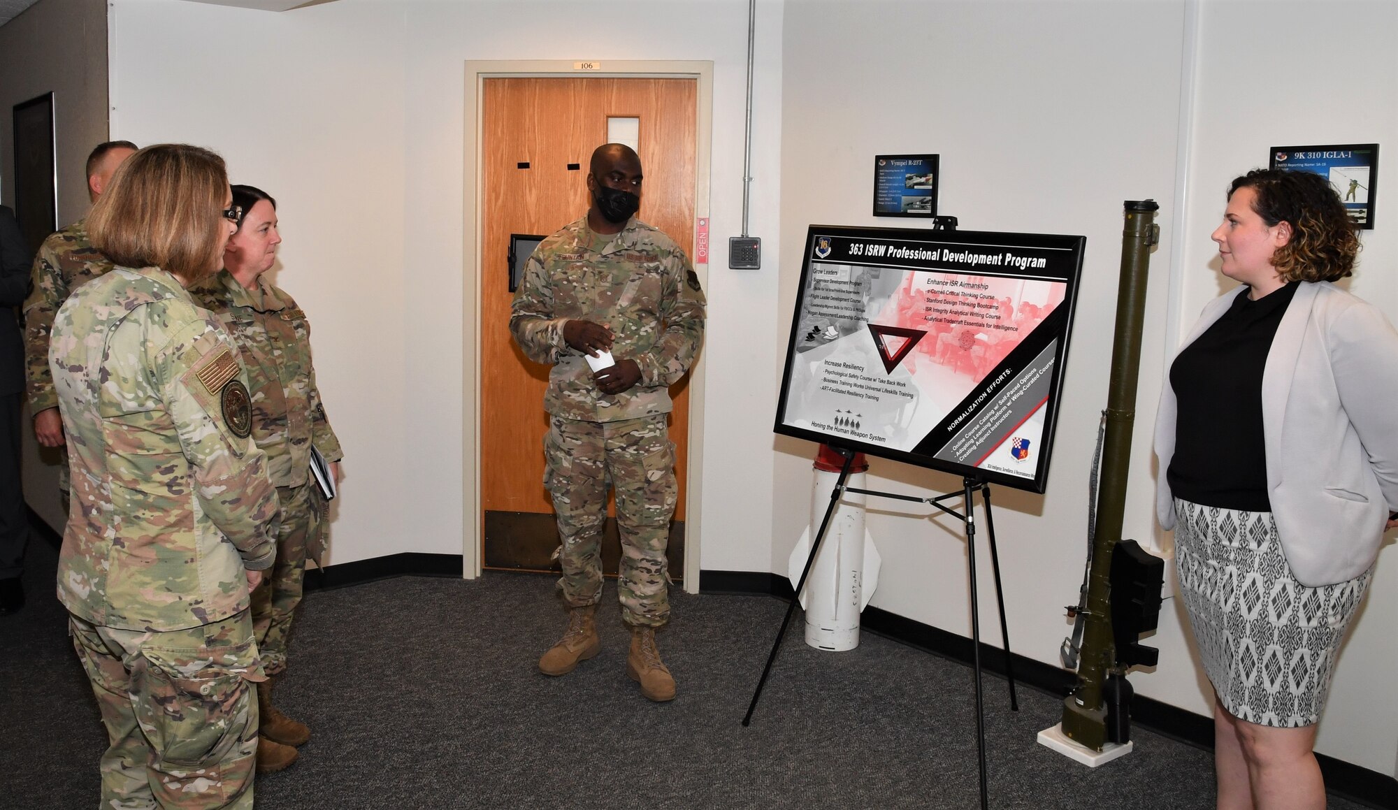 Several Airmen in uniform and one civilian stand in front a presentation board.