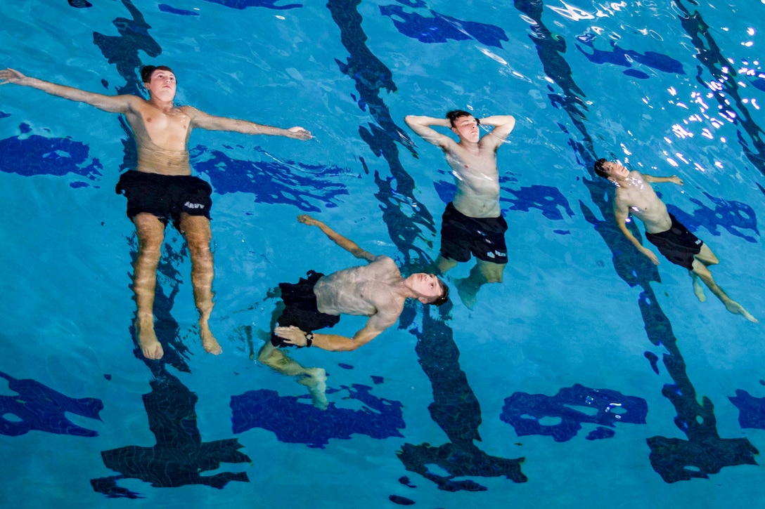 Four midshipmen float on their backs in a pool.