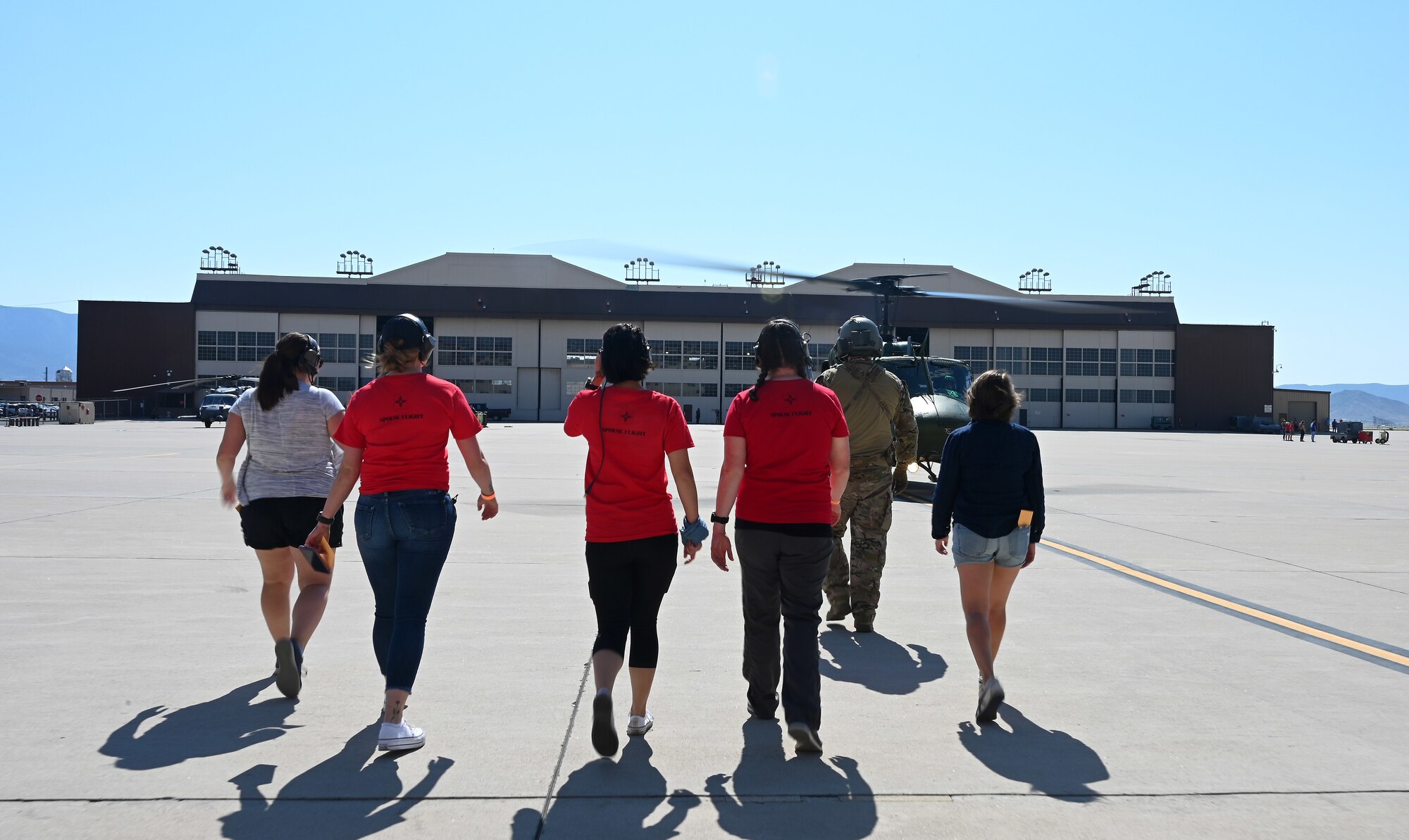 Individuals walking on a flightline toward an aircraft.