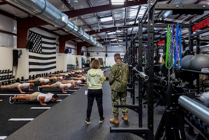 New fitness facility pictured with flight of students performing pushups while 2 people observe.