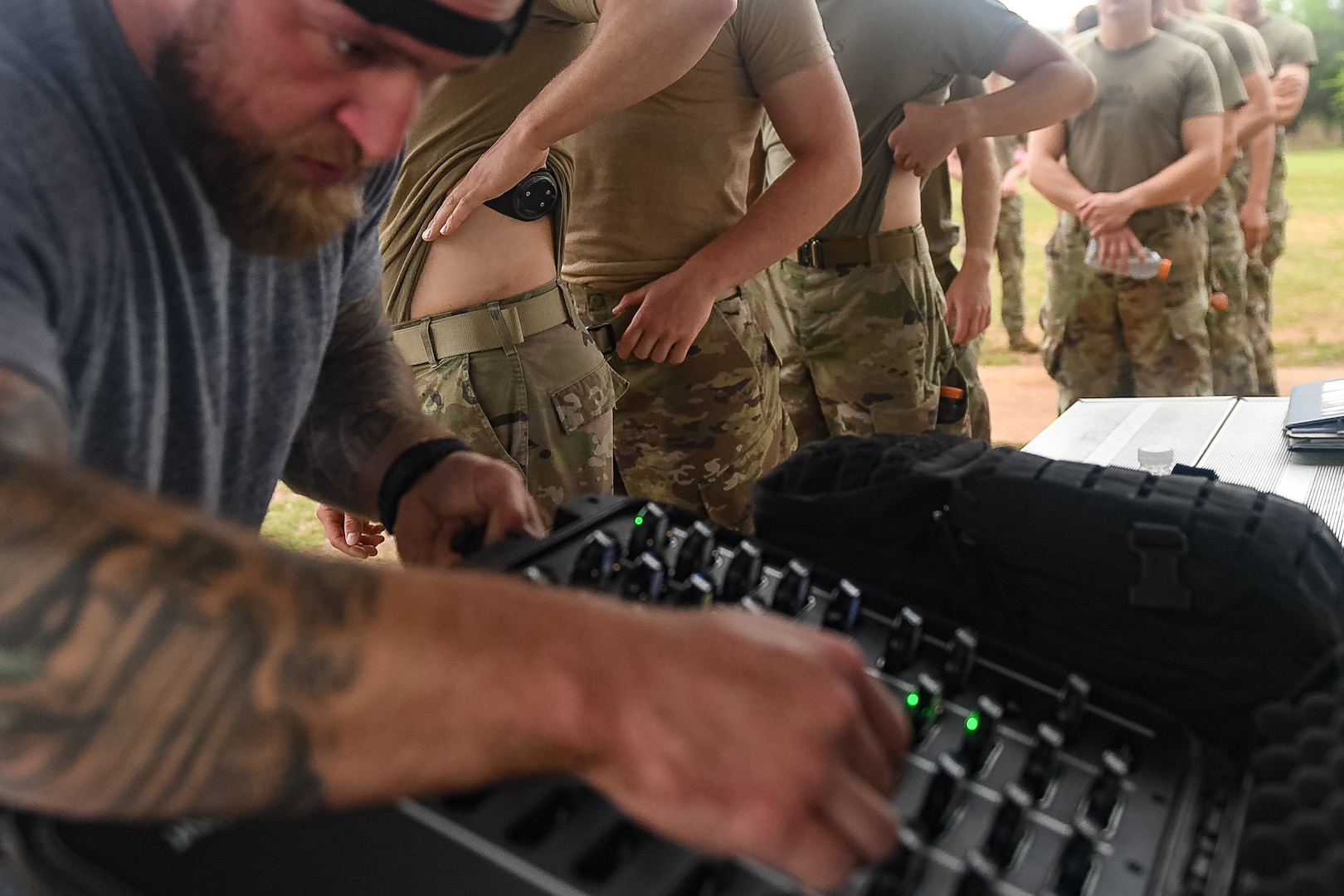 Air Force Civilian employee picking up a wearable computer device to attach to one of the training students behind him.