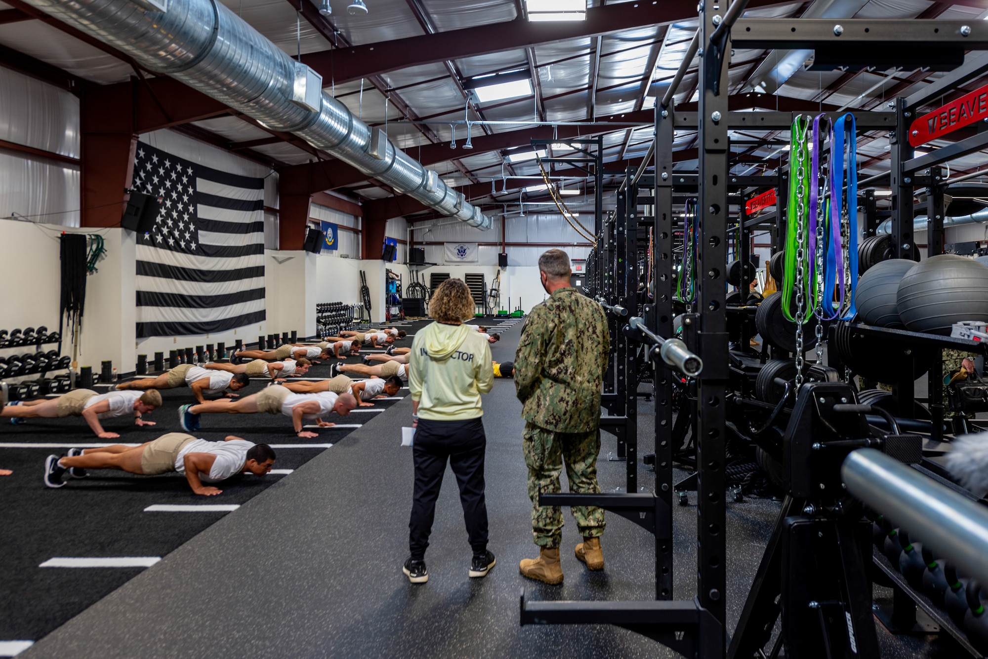 New fitness facility pictured with flight of students performing pushups while 2 people observe.