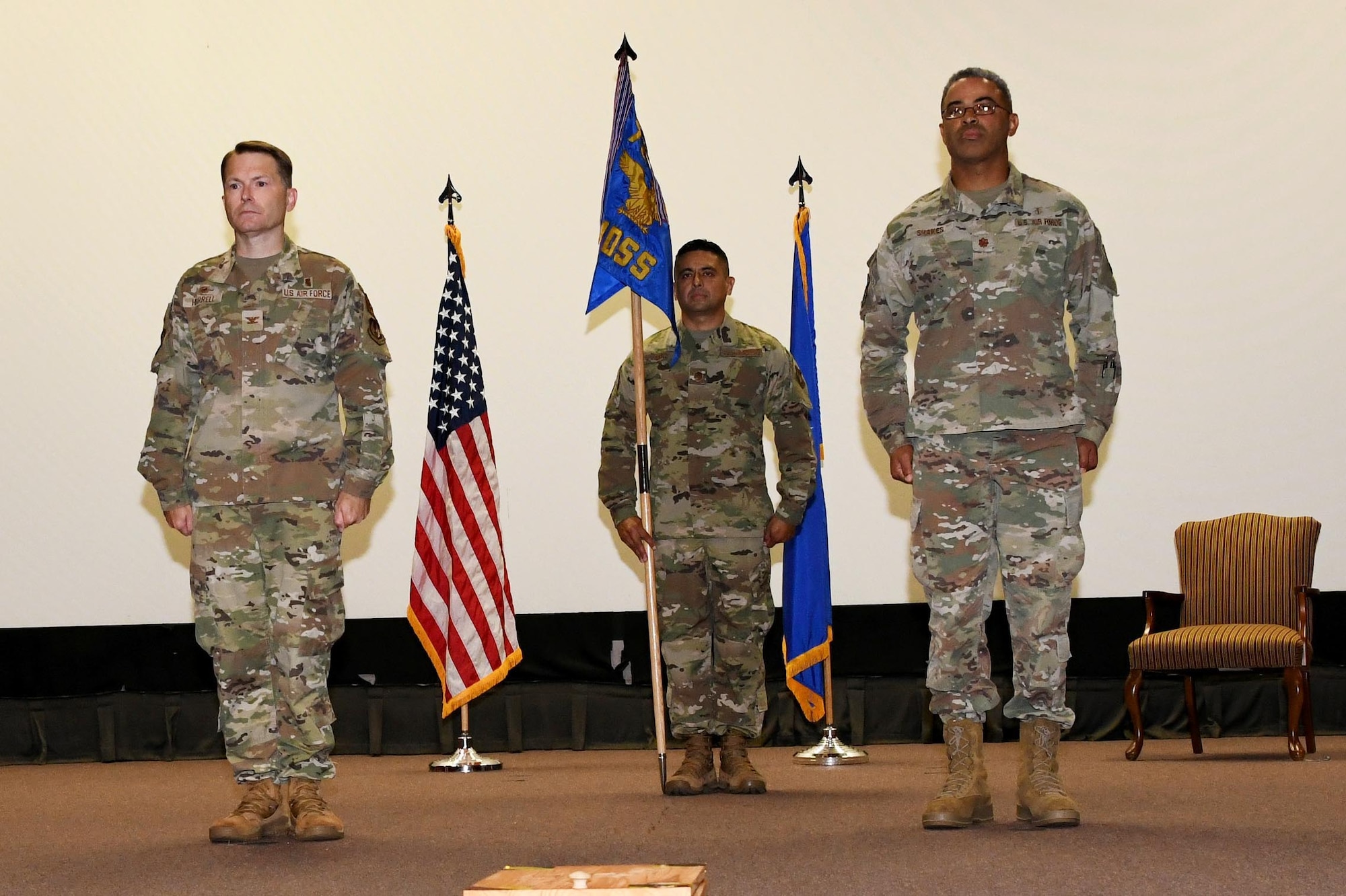 Photo shows three Airmen standing at attention on the stage while presenting a guidon.