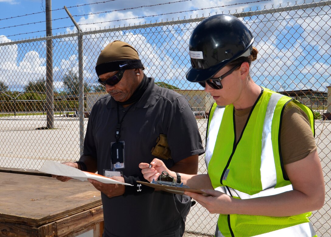 A woman and man go over a checklist in front of a fence.