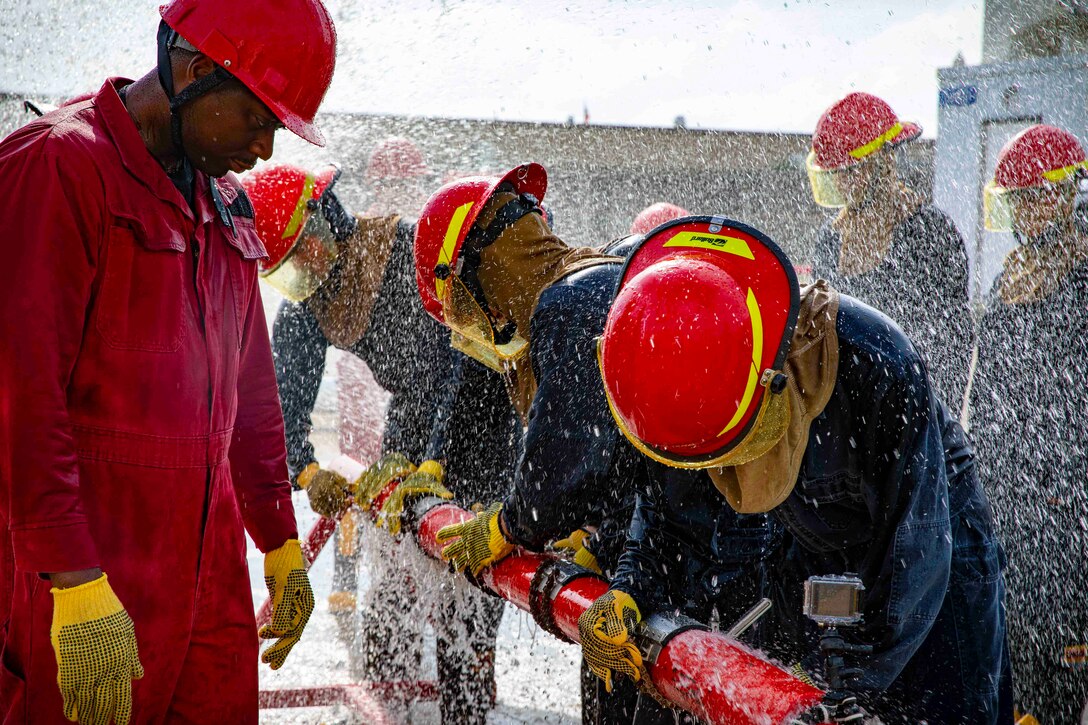 Midshipmen work on a leaky pipe as a sailor watches.