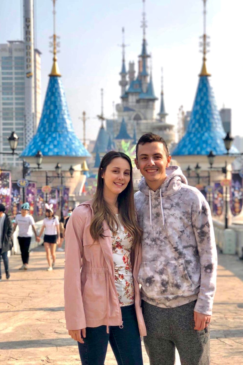 A smiling couple stands for a photo in front of a building with turrets with dramatic turquoise roofs.