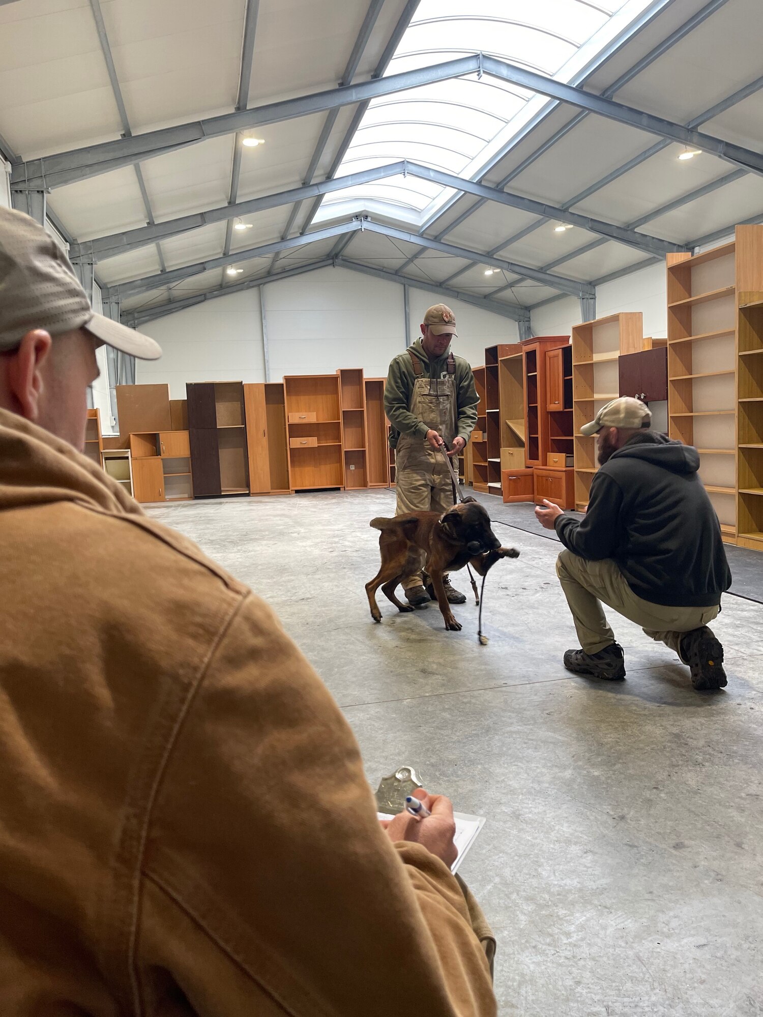 Man crouches down in front of dog being held by trainer.