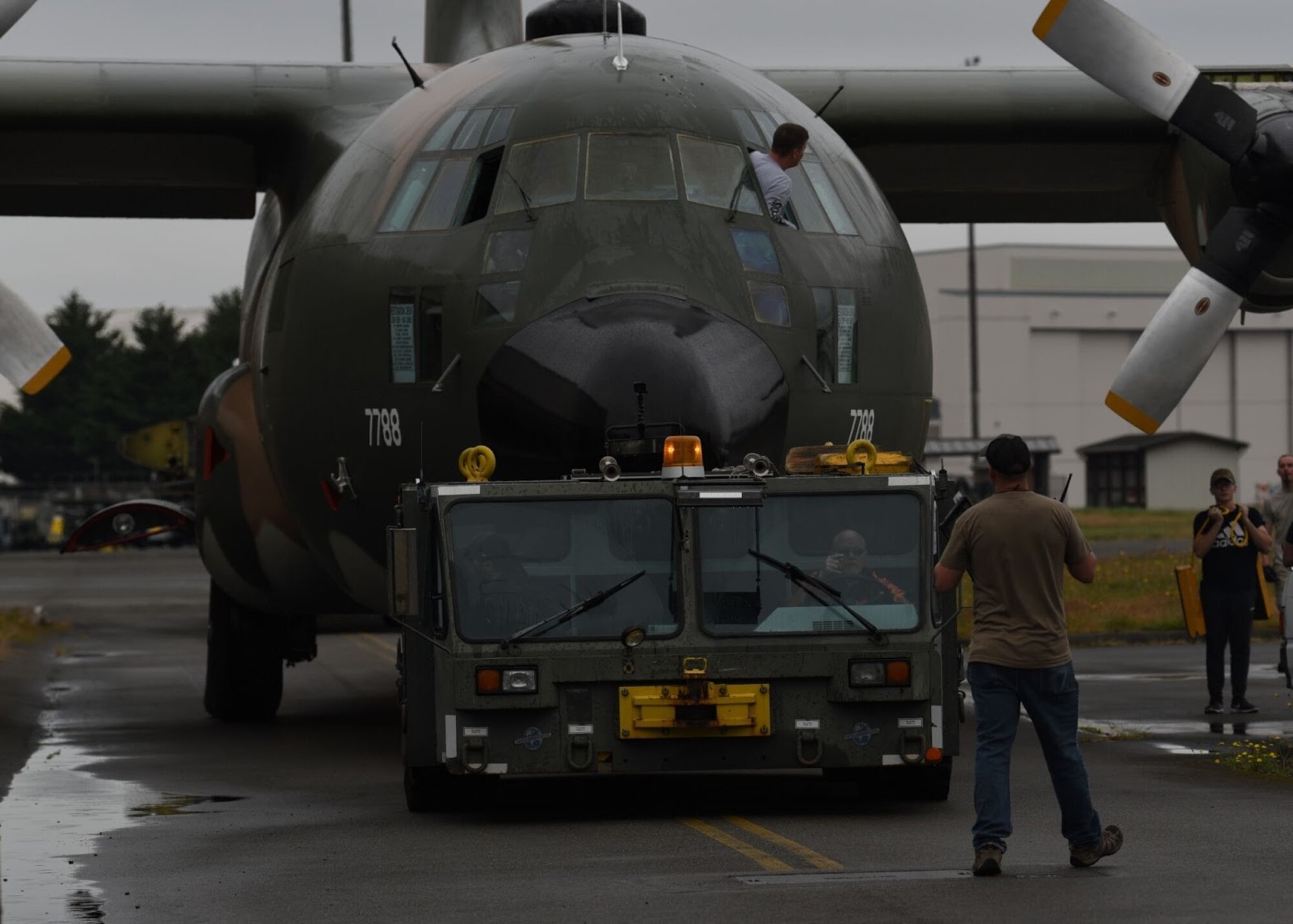 U.S. Air Force Senior Master Sgt. Joshua Pechacek, 62nd Aircraft Maintenance Squadron superintendent, guides a towing vehicle driver while he tows a C-130E Hercules at Joint Base Lewis-McChord, Washington, June 13, 2021. The 62nd AMXS worked alongside several other units in order to coordinate and carry out the successful removal of the C-130’s wings, engine, fuel tanks, lower antennas and landing gear doors so the aircraft could be towed down the McChord Field flightline and put on display after restoration. The C-130 was restored by volunteers and will be the newest addition to the aircraft of McChord Air Museum on Heritage Hill. (U.S. Air Force photo by Senior Airman Zoe Thacker)