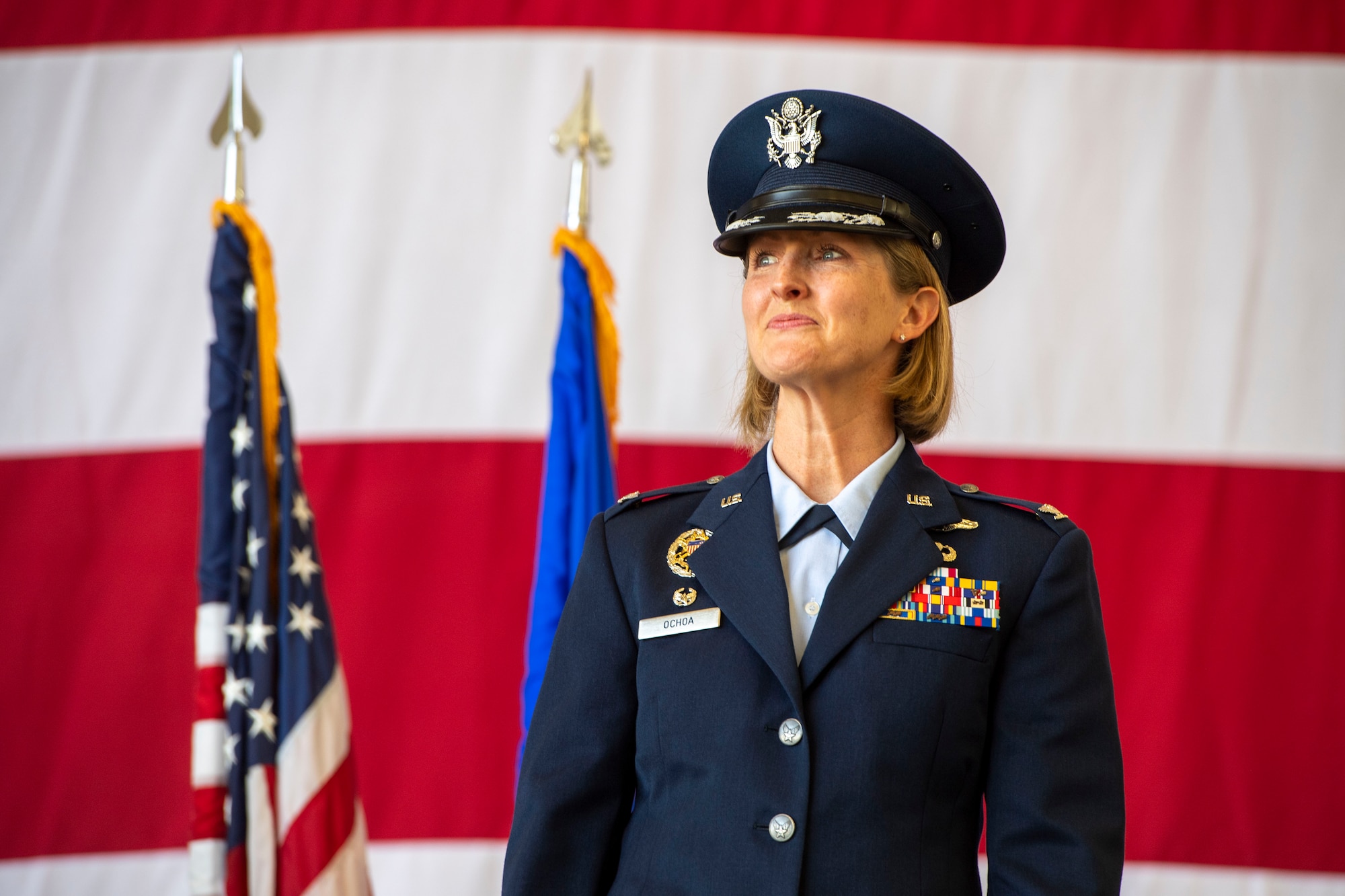 A female Airmen stands in front of the flags after assuming command.