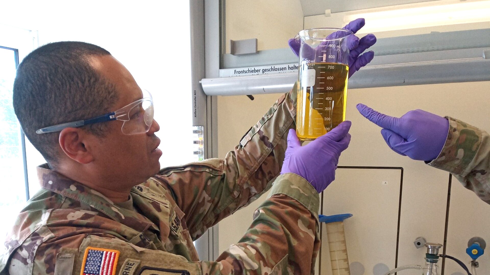 A military officer in uniform looks at a sample of fuel