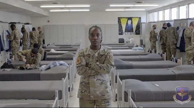 Staff Sgt. Alexandria Washington stands with her arms crossed while trainees are at their lockers in the background.