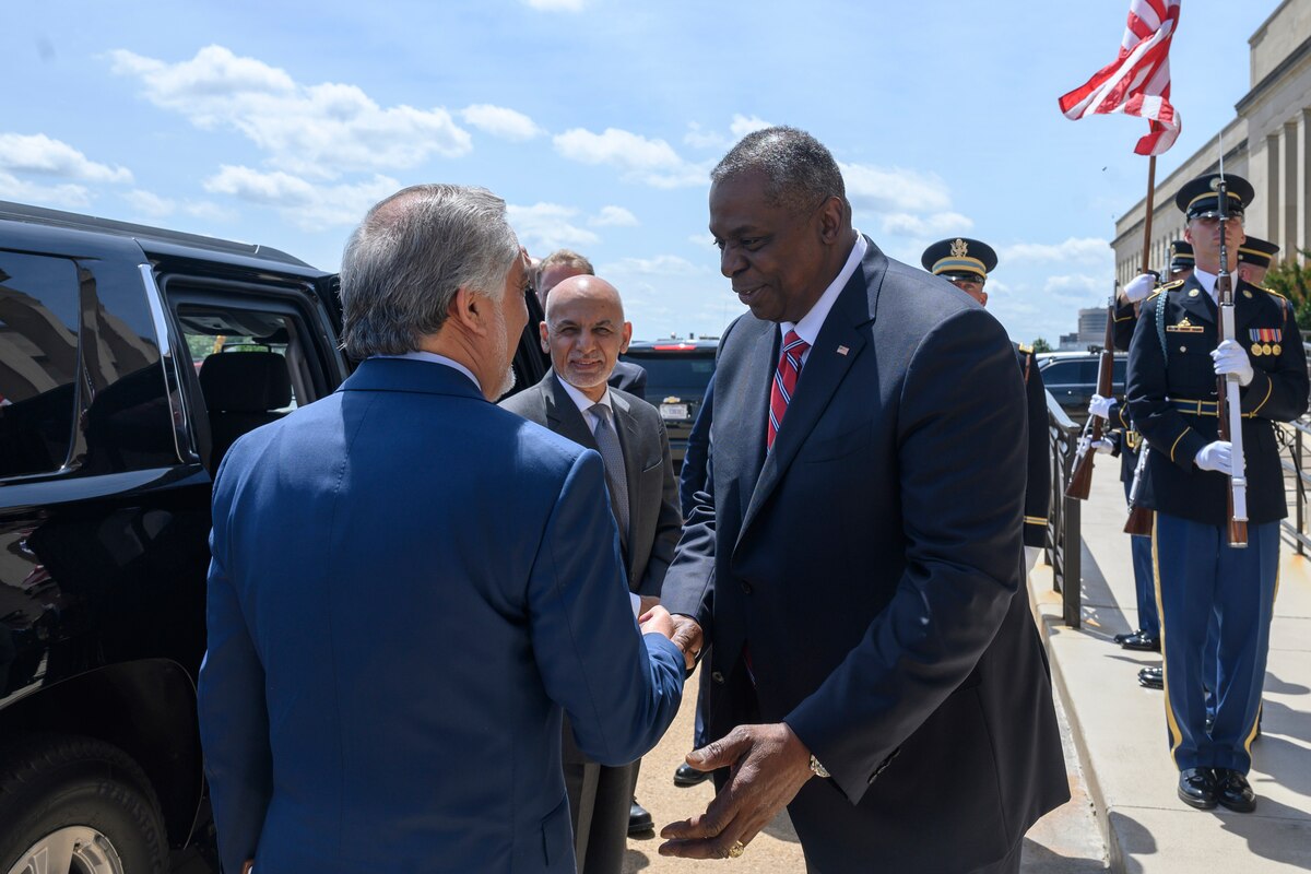 Secretary of Defense Lloyd J. Austin III shakes hands with one official as another stands by.