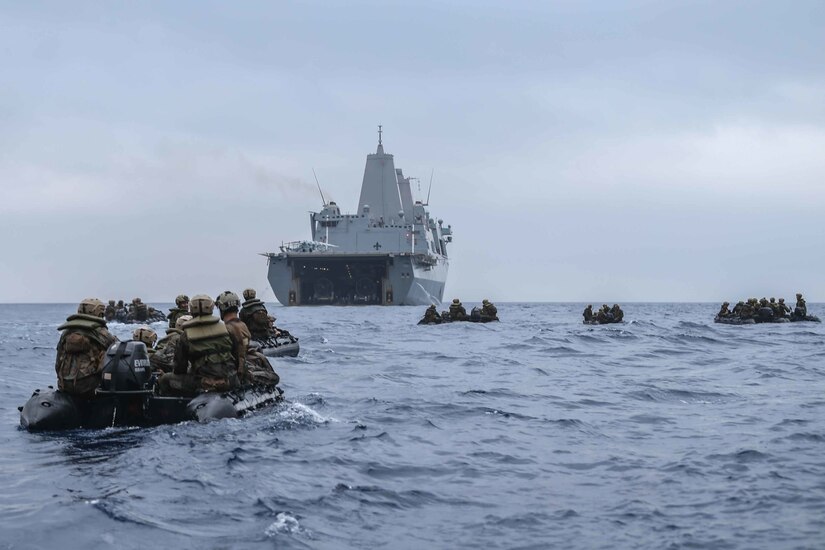Marines travel in small inflatable boats toward a large ship.