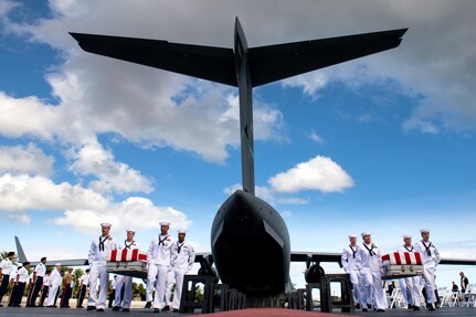 Service members carry flag-draped caskets on a flightline by an open aircraft.