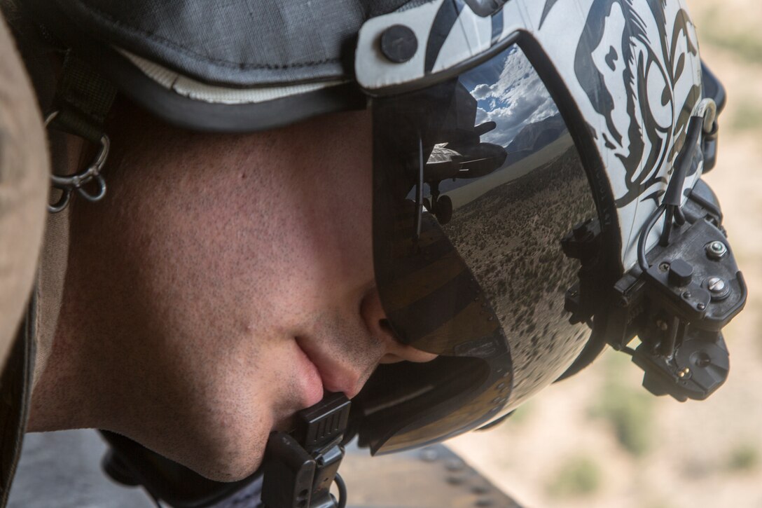 A Marine wearing a helmet and goggles looks downward.