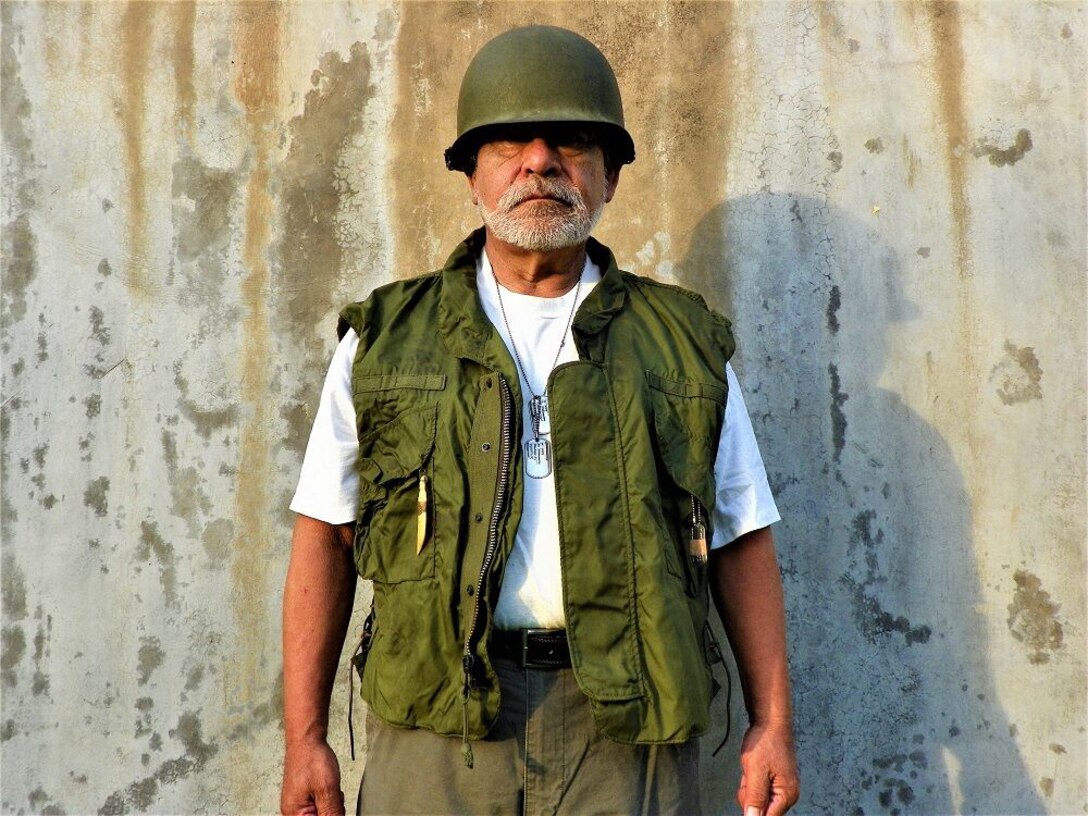 A man in a military helmet and vest stands for a photo.