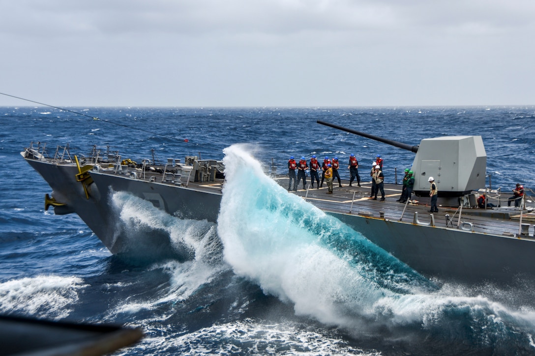 A wave crashes into a ship as it transits a body of water.