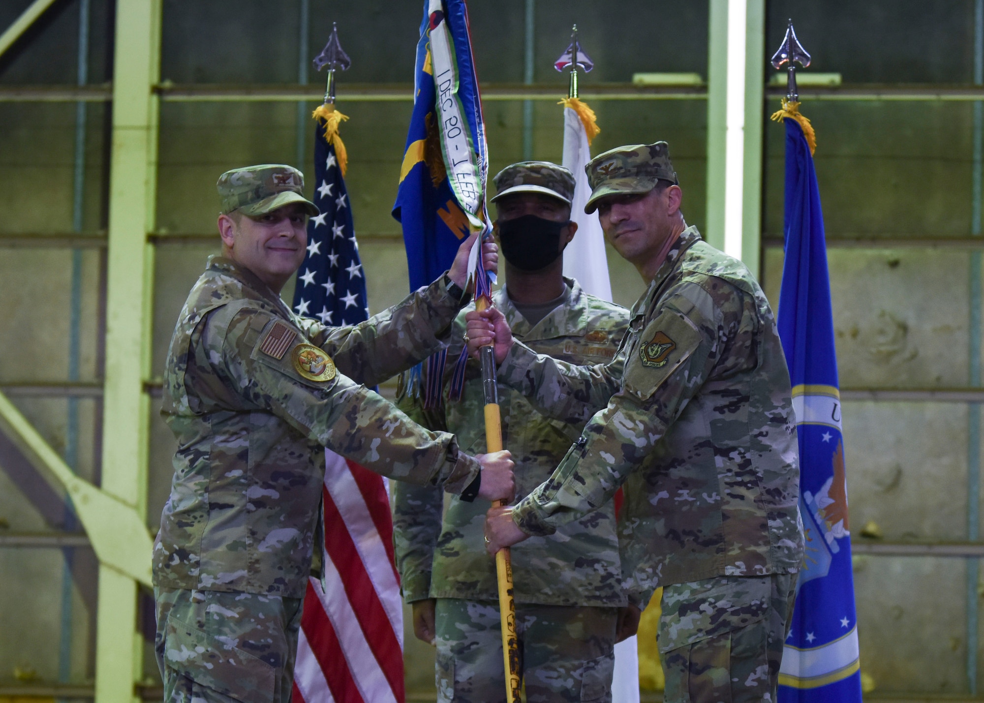Two military members hold a guidon looking into the camera in front of another military member.