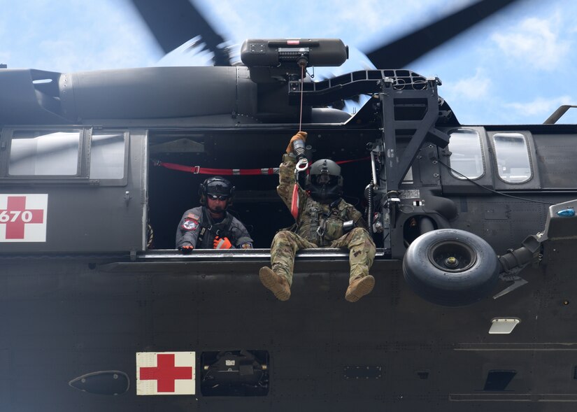 Guardsman peer out the side of a helicopter as it hovers in the air.
