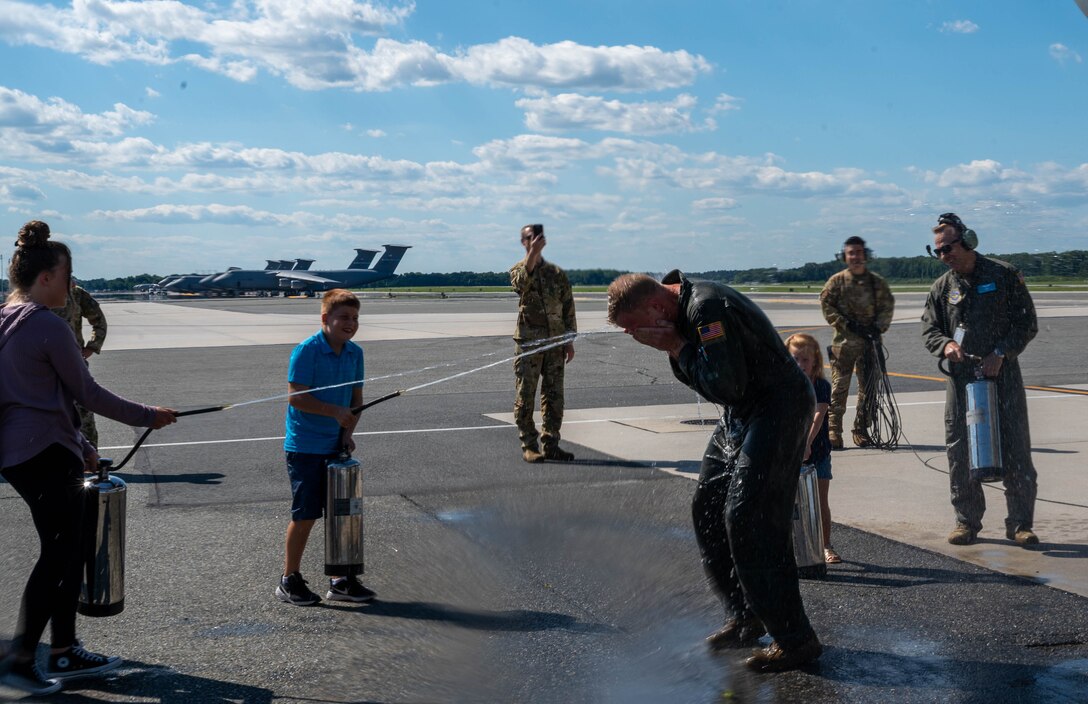 Lt. Col. John Habbestad, 9th Airlift Squadron commander, is sprayed with water by his family to celebrate his final C-5M Super Galaxy flight as the 9th AS commander at Dover Air Force Base, Delaware, June 23, 2021. Habbestad served as commander for two years. (U.S. Air Force photo by Senior Airman Faith Schaefer)