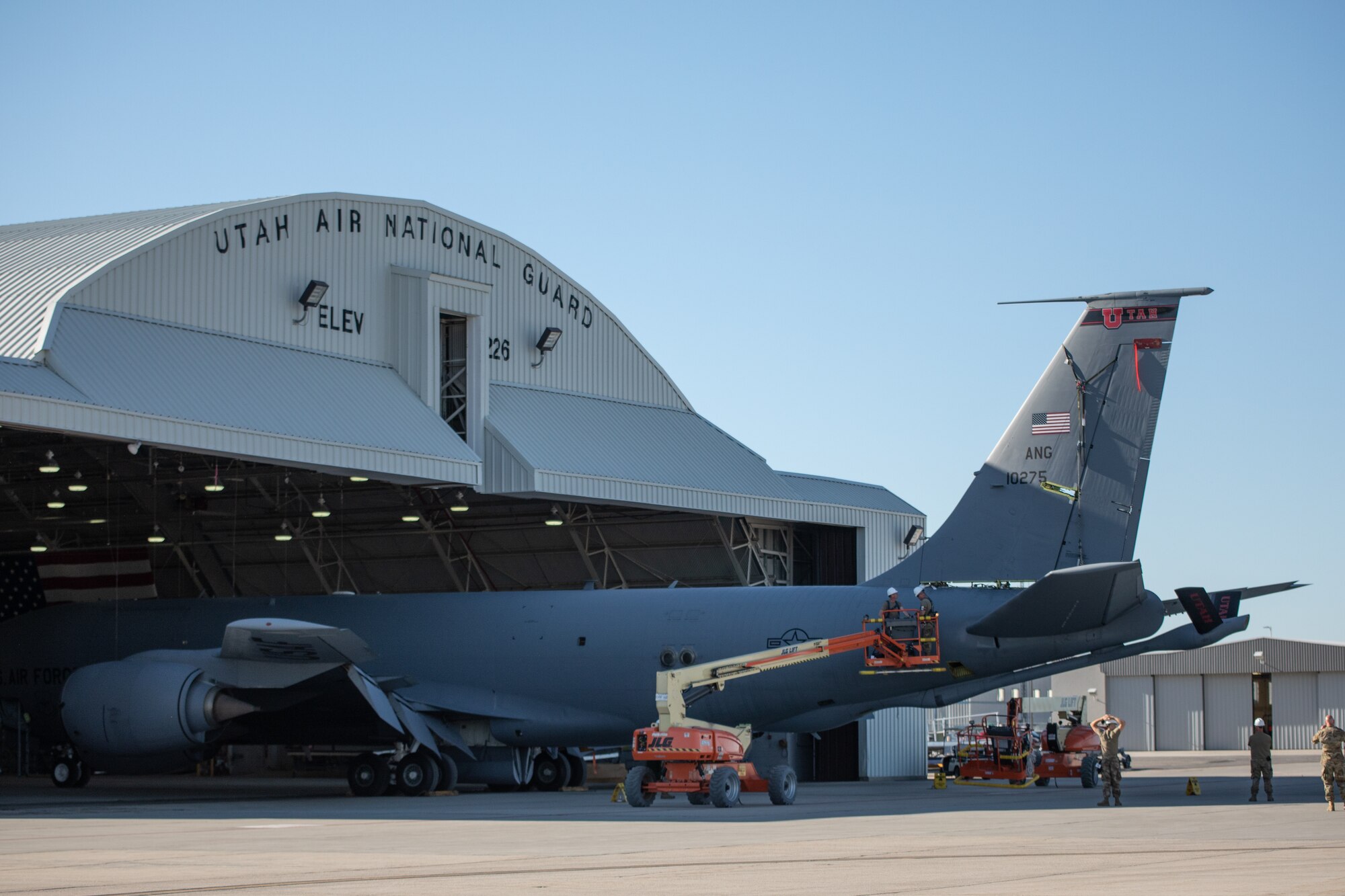 Air Force members remove the tail off of a KC-135 Stratotanker. They are strapped in harnesses and are working off a lift truck.