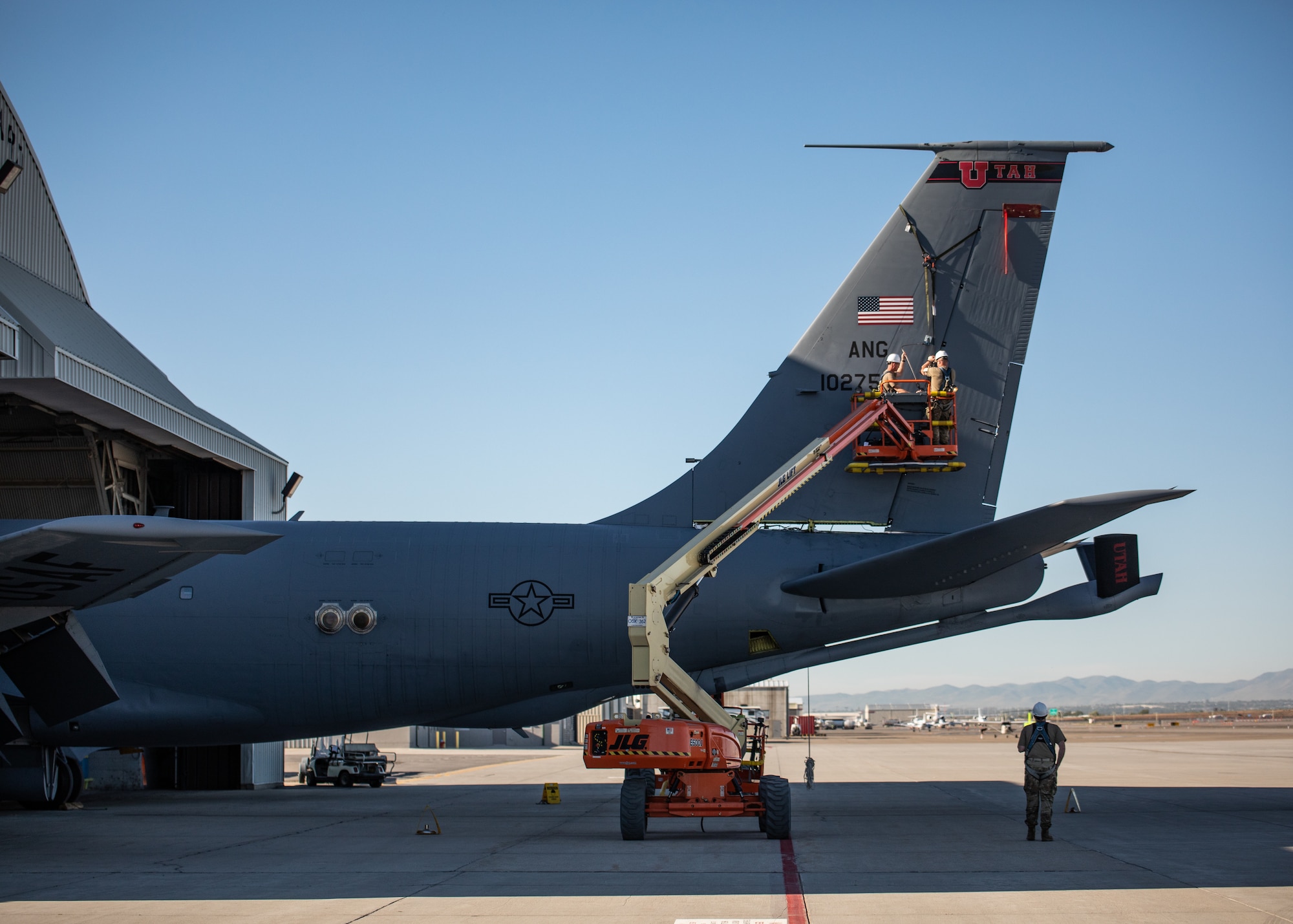 Air Force members remove the tail off of a KC-135 Stratotanker. They are strapped in harnesses and are working off a lift truck.