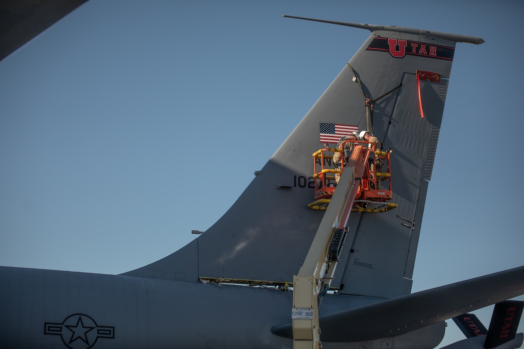 Air Force members remove the tail off of a KC-135 Stratotanker. They are strapped in harnesses and are working off a lift truck.