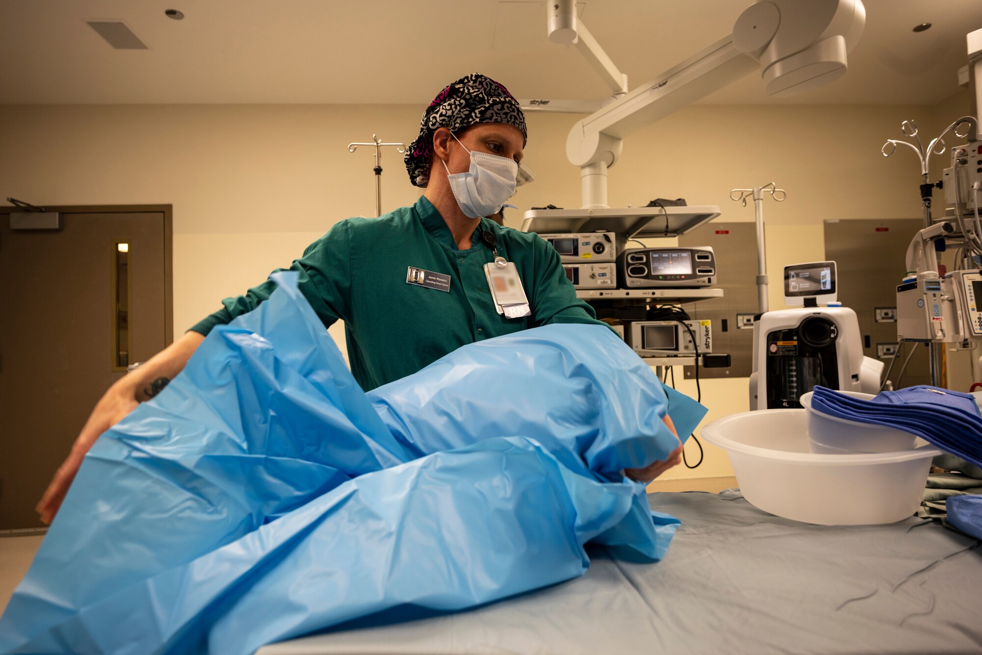 A woman wearing nurse scrubs preps an operating room table.