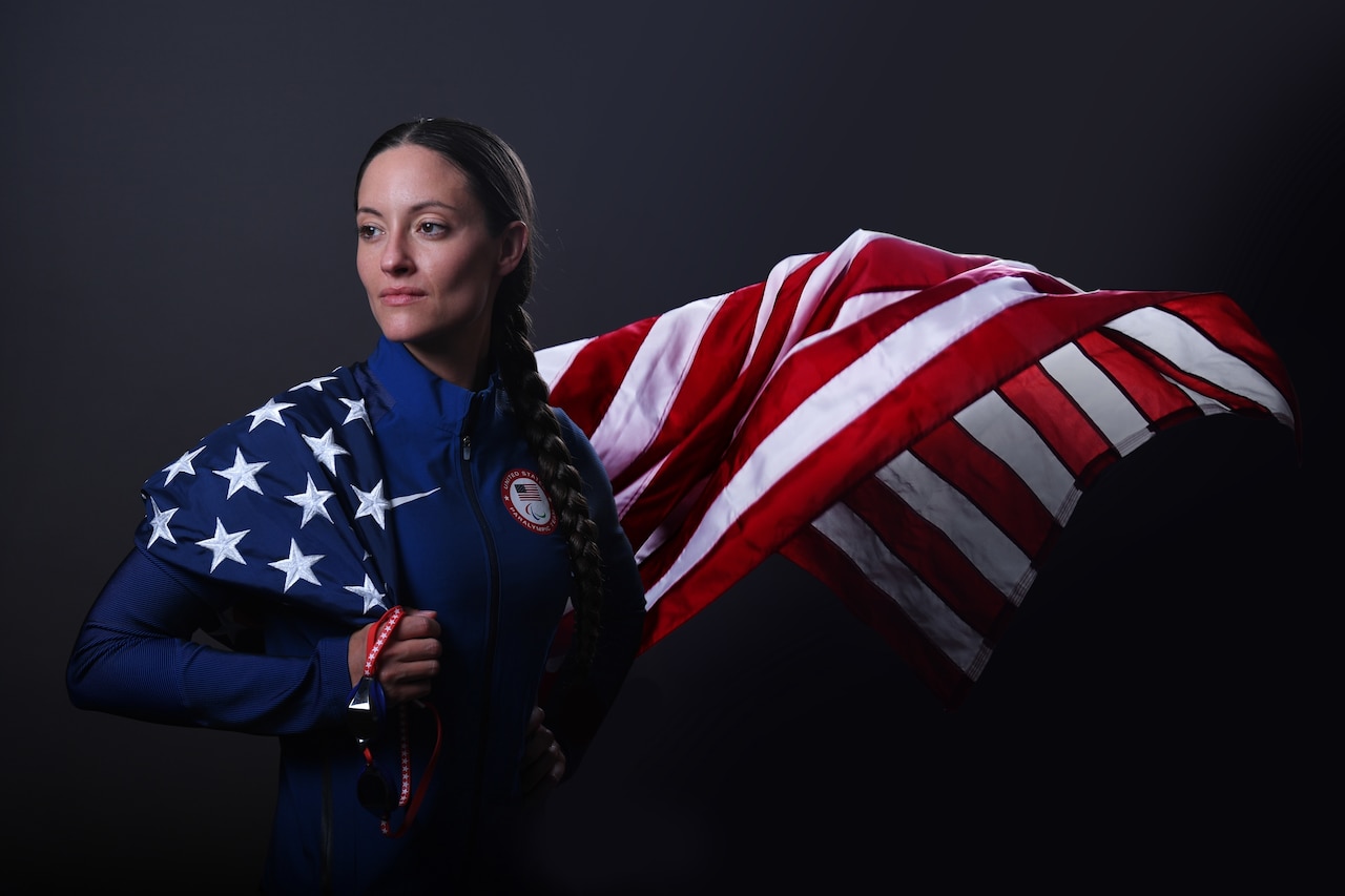 A soldier poses for a photo while having an American flag draped over her.
