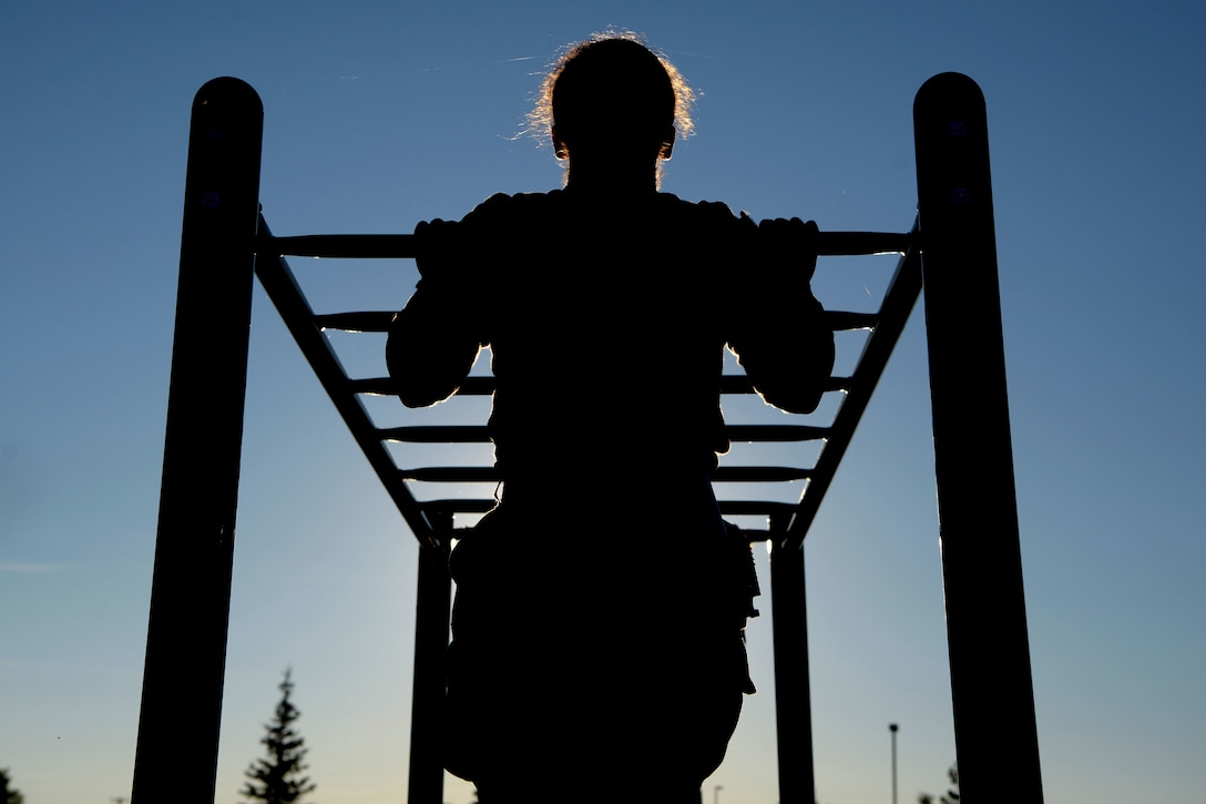 An airmen performs a pullup as shown in silhouette.