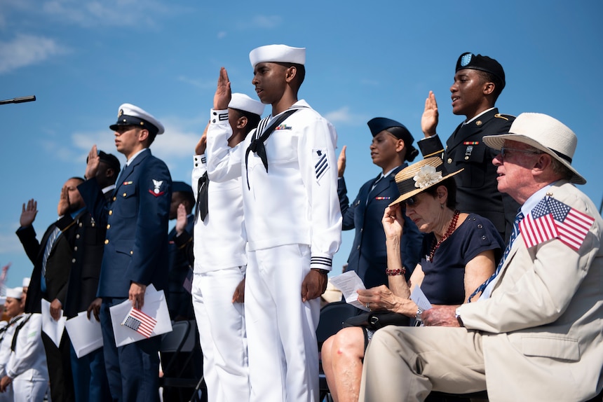 Soldiers, Sailors, Airmen, a Coast Guardsman and an Army veteran raise their right hands as they recite the Oath of Allegiance during a naturalization ceremony aboard USS Constitution.