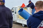 Man tips over a container of water to demonstrate what a 30 gallon spill looks like to a small group of people at Kirtland, AFB.