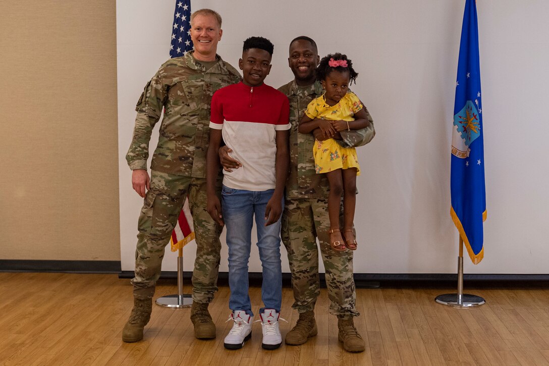 Photo of an Airman posing with another Airman and his children