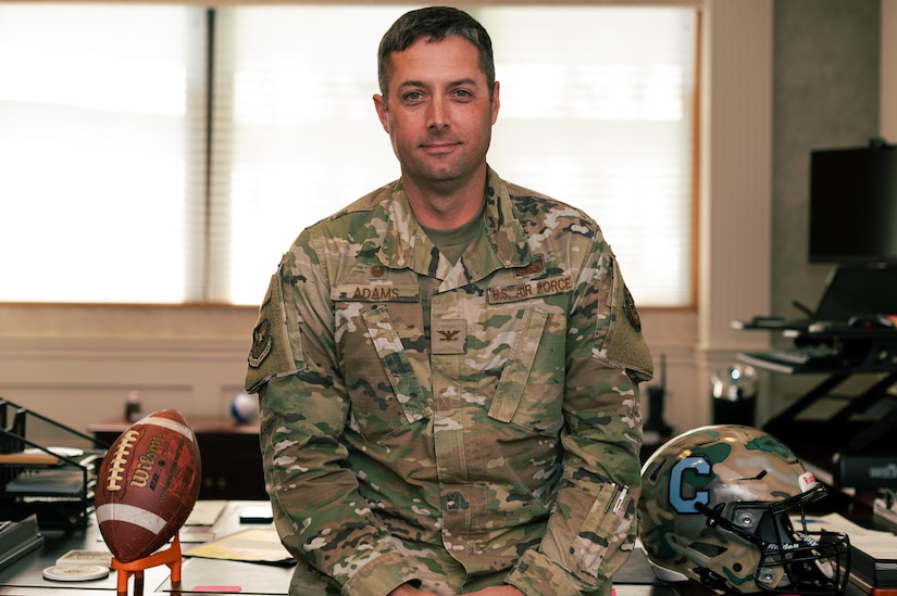 U.S. Air Force Col. Wes Adams, Joint Base McGuire-Dix-Lakehurst commander and 87th Air Base Wing commander, poses for a photo. On his desk lay papers, a football, and Citadel football helmet.