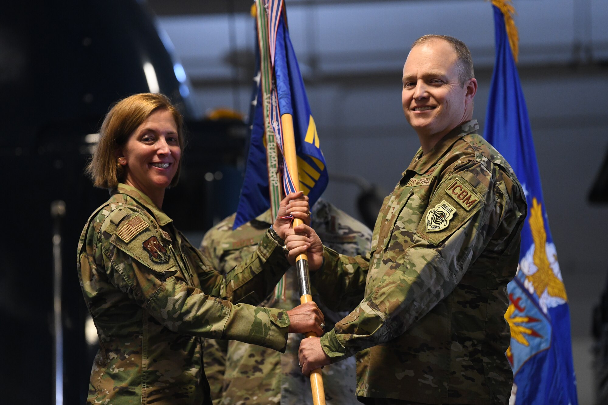 Col. Catherine Barrington, Commander of the 90th Missile Wing, passes the guidon to Col. Michael Power, the incoming commander of the 90th Maintenance Group, during the 90 MXG Change of Command Ceremony on F.E. Warren Air Force Base, Wyoming, on June 30, 2021. The change of command ceremony signifies the transition of command from Col. Brian Rico, the outgoing commander of 90 MXG, to Power. (U.S. Air Force photo by Airman 1st Class Frazier)