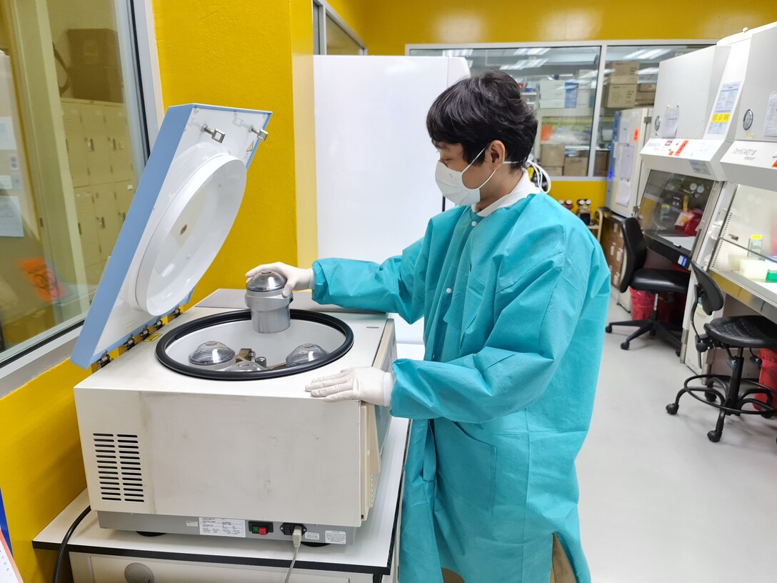 Scientist in laboratory coat removes sample from container.