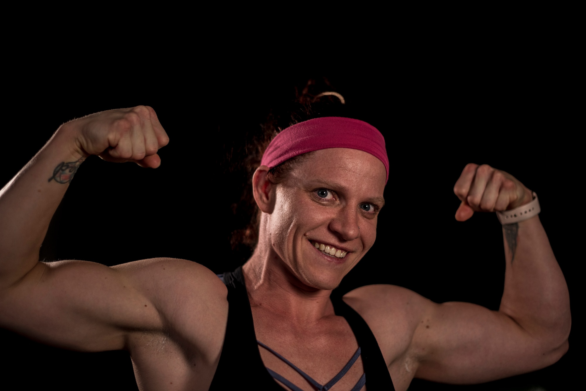 A woman wearing a work out top flexes her arms for the camera with a big smile on her face.