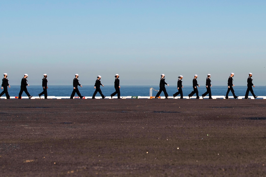 Sailors walk in a line on a ship.
