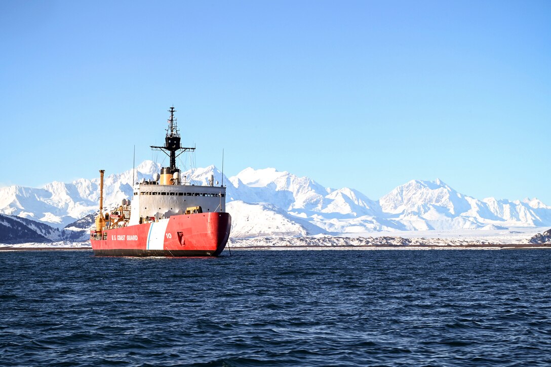 A ship sits at anchor with snowy mountains in the background.