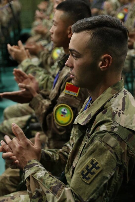 Soldiers clap as they sit side-by-side in rows.