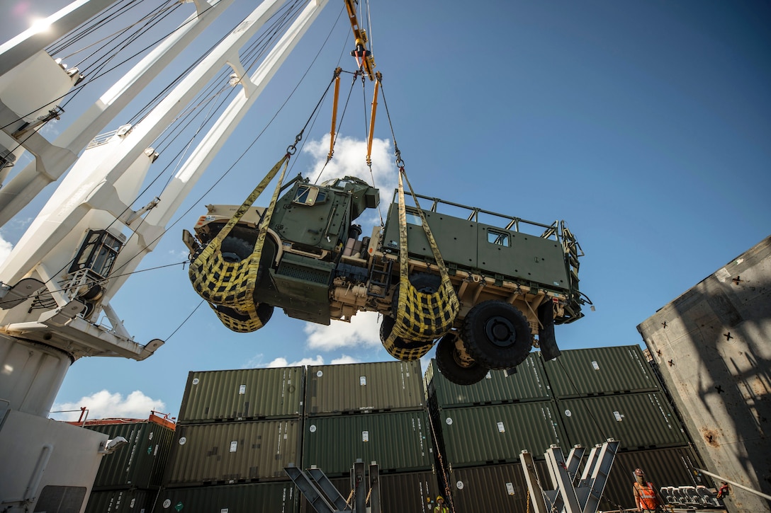 Marines and sailors lift a vehicle on a ship.