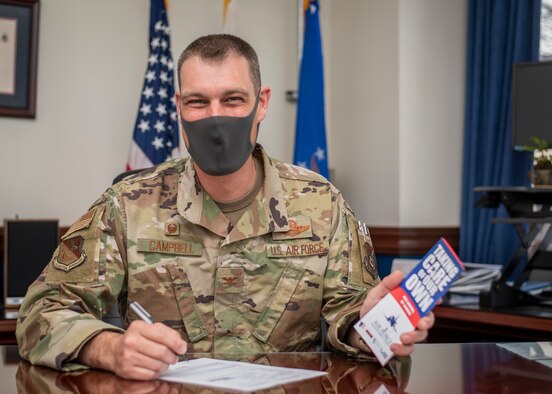 Col. Andrew Campbell sits at a desk, signing a donation