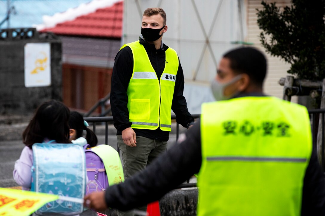 U.S. Marine Corps Lance Cpl. Kyle Knepper, center, and Lance Cpl. James Cruz, right, heavy equipment operators with 9th Engineer Support Battalion, 3rd Marine Logistics Group, act as crossing guards while students cross a crosswalk at Kitatama Elementary School, Chatan, Okinawa, Japan Jan. 7, 2021. Every Tuesday and Thursday, military community volunteers serve as crossing guards to assist elementary students and staff crossing a busy neighborhood intersection. The volunteers received letters of appreciation for their work from the Kitatama Community Center.