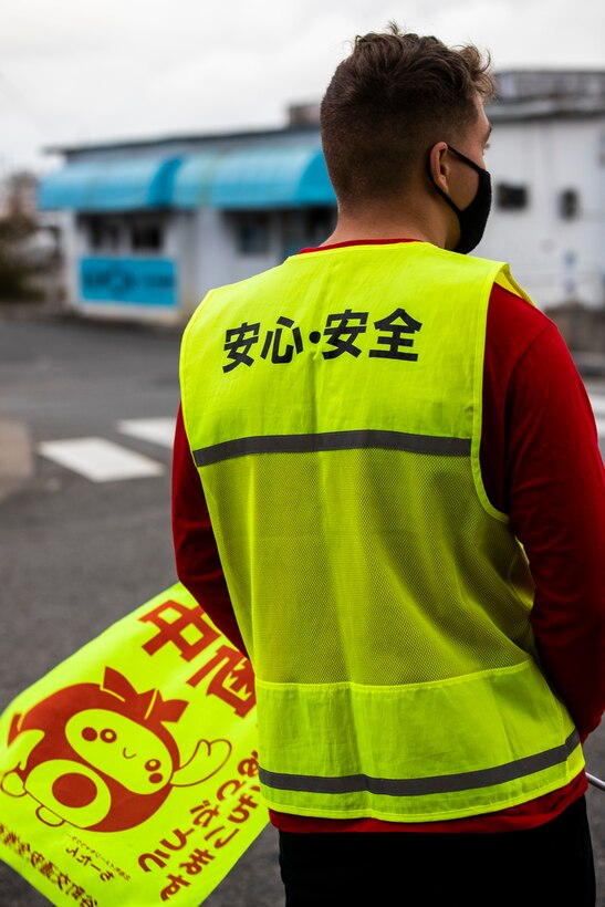 U.S. Marine Corps Lance Cpl. Carson Cleasby, a heavy equipment operator with 9th Engineer Support Battalion, 3rd Marine Logistics Group, waits for students of Kitatama Elementary School to approach a crosswalk at Kitatama Elementary School, Chatan, Okinawa, Japan Jan. 7, 2021. Every Tuesday and Thursday, military community volunteers serve as crossing guards to assist elementary students and staff crossing a busy neighborhood intersection. The volunteers received letters of appreciation for their work from the Kitatama Community Center. (U.S. Marine Corps photo by Cpl. Ryan H. Pulliam)