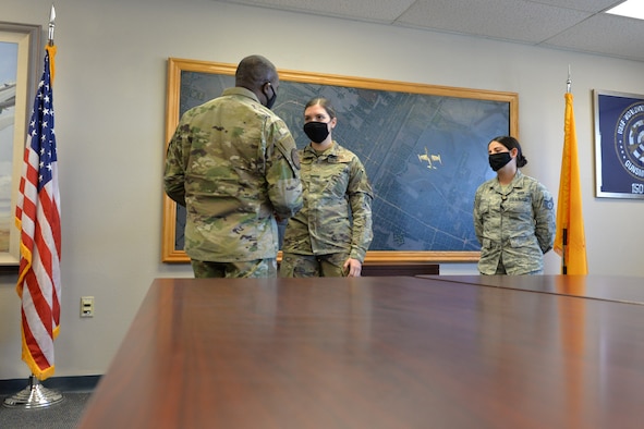 Command Chief Master Sgt. Maurice Williams gives a coin to Senior Airman Shelby Snow as her supervisor watches in a conference room setting with an American flag to the left and the New Mexico state flag to the right