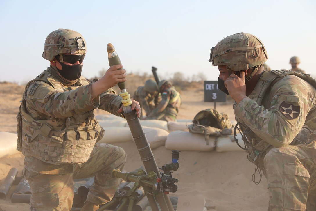 Two soldiers load a mortar firing while others do the same in the distance.