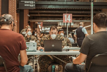 A hospital corpsman with assists local community members through the check-in process to receive their COVID-19 vaccine.