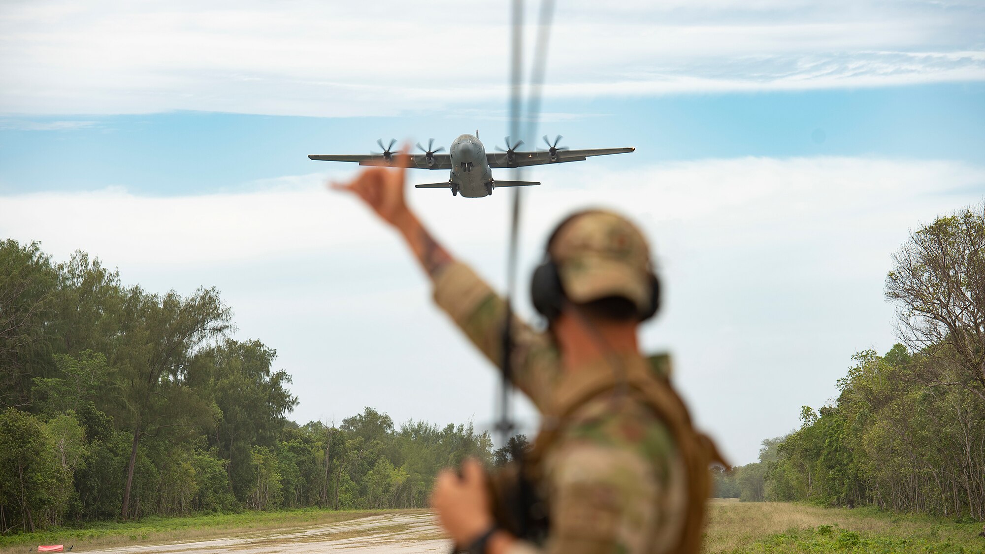 U.S. Air Force Capt. Gene Walker, 36th Contingency Response Squadron assistant director of operations, waves on a C-130J Super Hercules from Yokota Air Base as it approaches the landing zone during Cope North 21, Feb. 11, 2021, on Angaur, Palau.