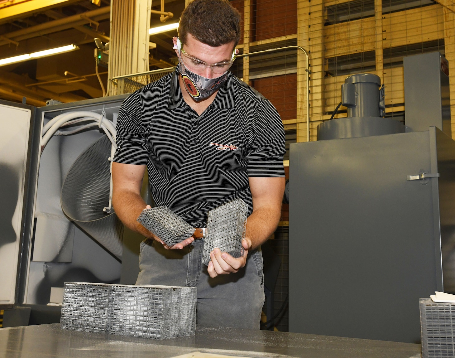 Fleet Readiness Center Southeast (FRCSE) mechanical engineer, Evan Grambling, removes 3D printed nasopharyngeal swab cages from the automated glass bead blaster after a timed blasting cycle.